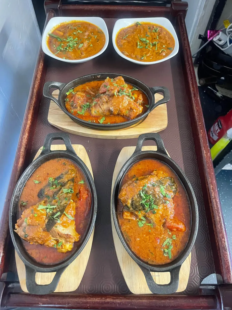 Our curries on the pass: two bowls and three cast-iron dishes of chicken on the bone in a red sauce with fresh coriander.