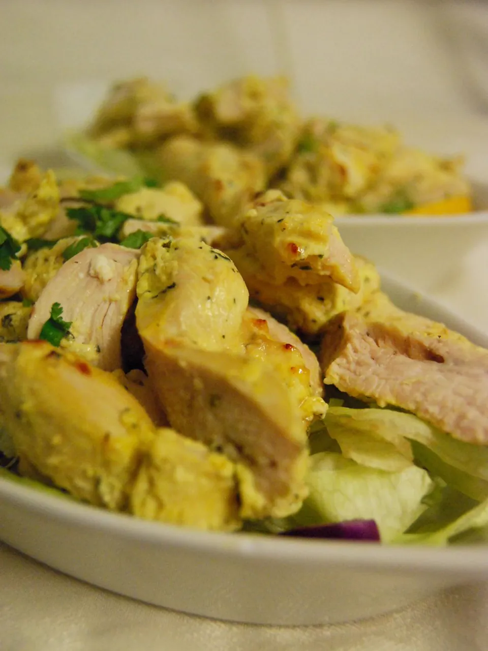 Pieces of marinated grilled chicken on lettuce in a white dish, with a second dish behind.