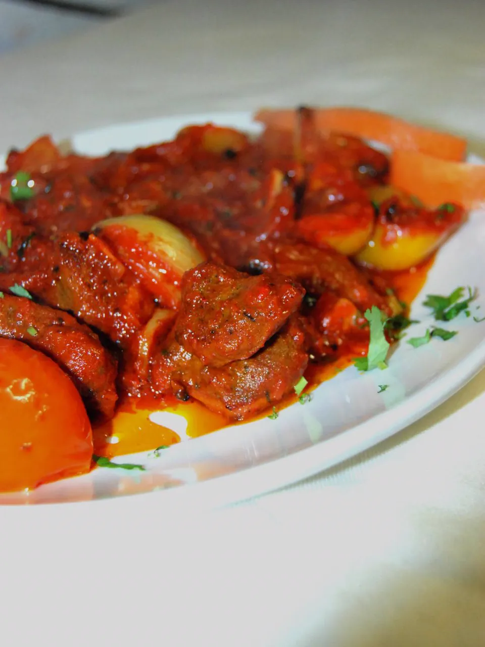 Pieces of meat in a red sauce with onion and tomato on a white plate, sprinkled with fresh coriander.